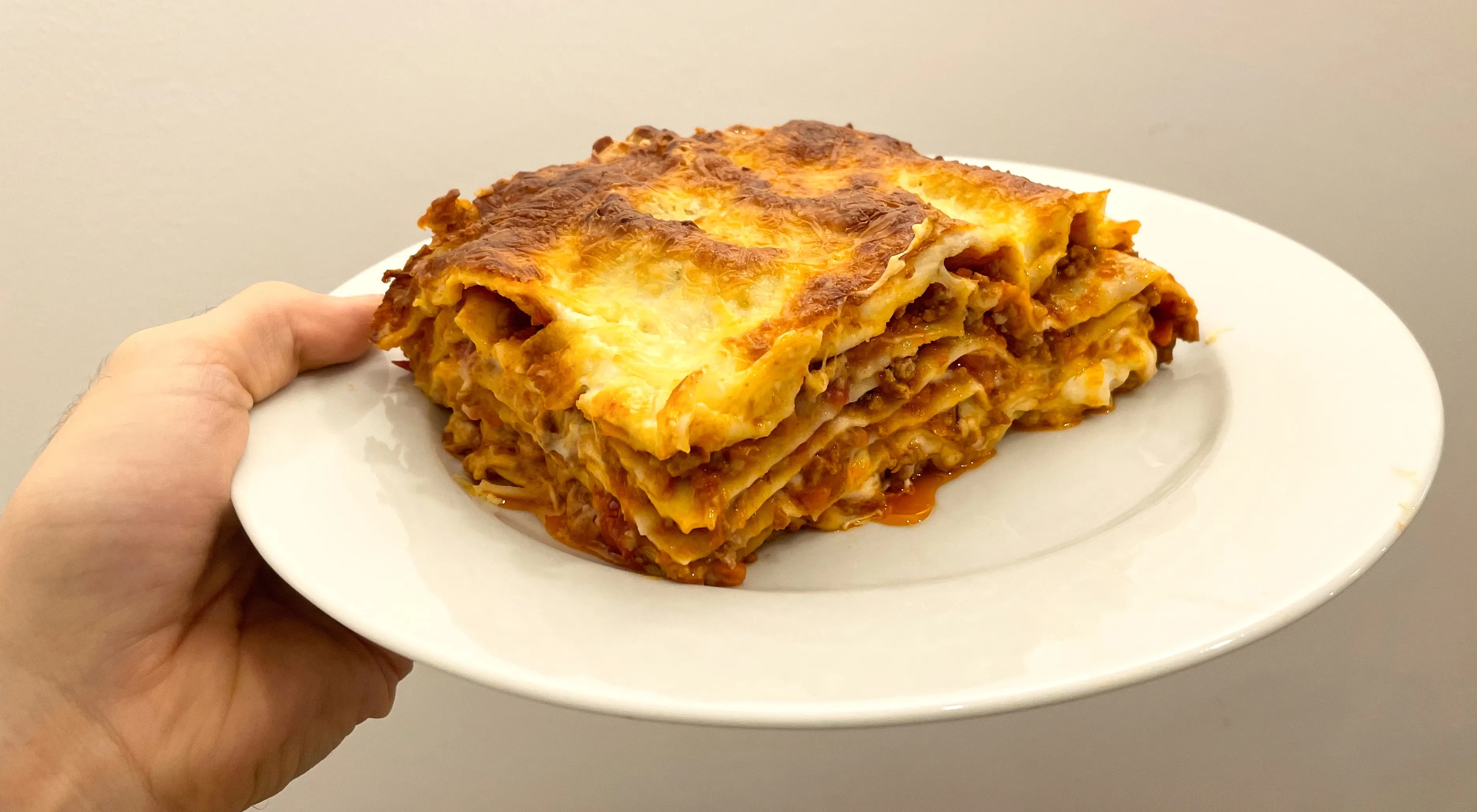 Abbildung eines fertig gebackenen Stücks Lasagne auf einem Teller vor einer weißen Wand